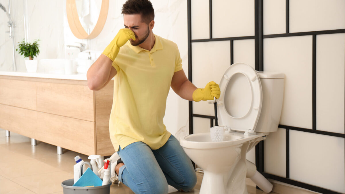 Young man feeling disgust while cleaning toilet bowl in bathroom