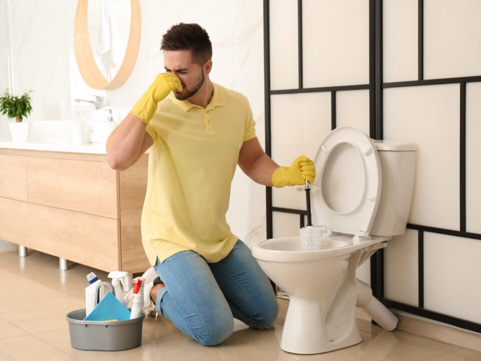 Young man feeling disgust while cleaning toilet bowl in bathroom